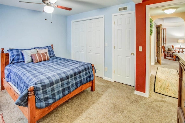 bedroom featuring visible vents, a closet, arched walkways, light colored carpet, and ceiling fan