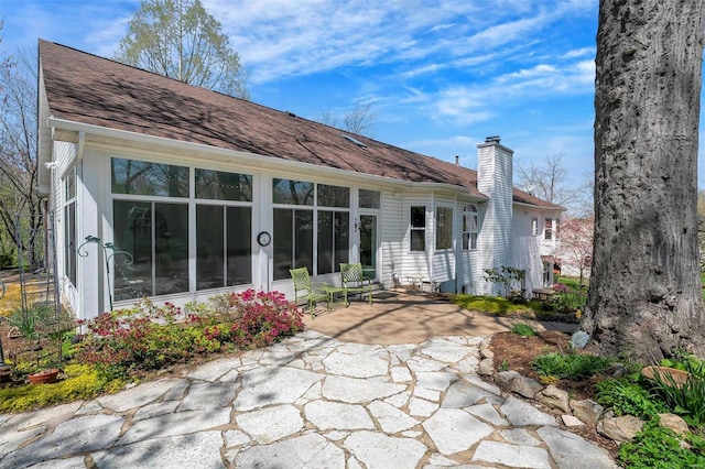 rear view of house with a chimney, roof with shingles, and a patio