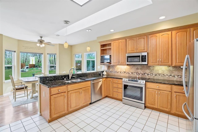 kitchen featuring tasteful backsplash, a sink, pendant lighting, a peninsula, and appliances with stainless steel finishes