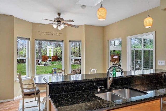 kitchen with dark stone countertops, pendant lighting, a sink, and light wood-style floors