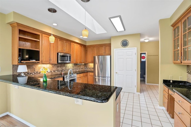 kitchen with dark stone countertops, decorative backsplash, glass insert cabinets, stainless steel appliances, and a peninsula