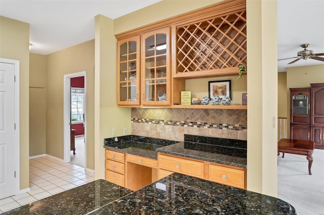 kitchen with dark stone counters, decorative backsplash, glass insert cabinets, ceiling fan, and light tile patterned floors