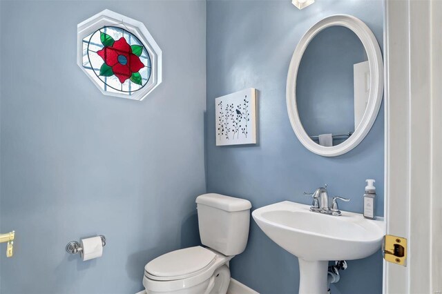 half bathroom with toilet, a sink, and baseboards