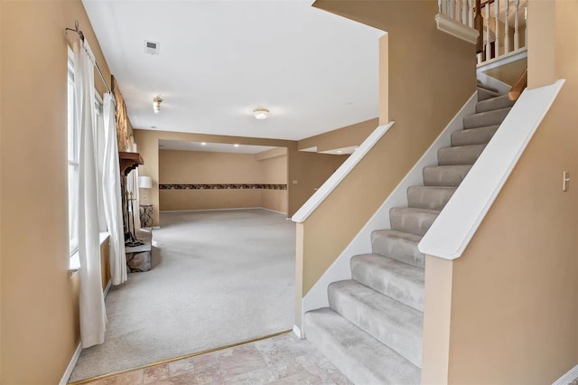 stairway with baseboards, stone finish floor, visible vents, and carpet