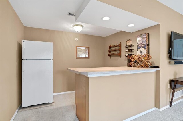 kitchen with a peninsula, visible vents, baseboards, freestanding refrigerator, and carpet