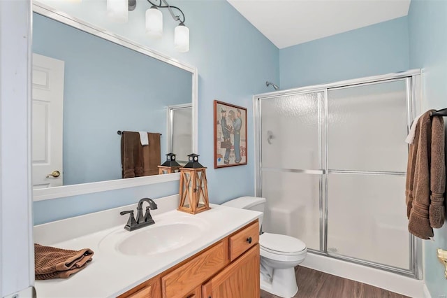 full bath featuring toilet, wood finished floors, vanity, and a stall shower