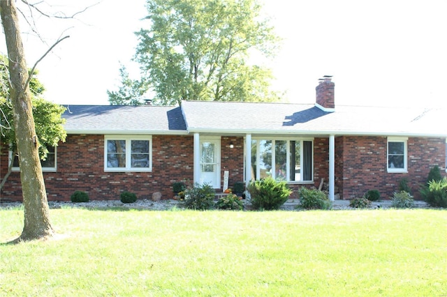 ranch-style home featuring a front yard, brick siding, a chimney, and roof with shingles