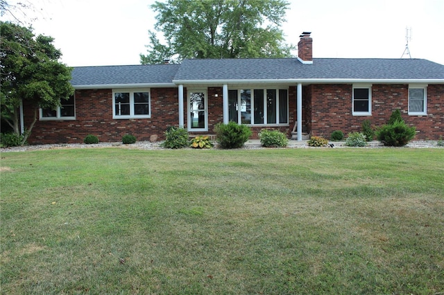 ranch-style home with roof with shingles, brick siding, a chimney, and a front yard