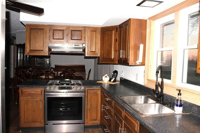 kitchen featuring dark countertops, brown cabinetry, a sink, under cabinet range hood, and stainless steel gas range oven