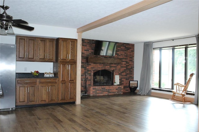 living room featuring a textured ceiling, dark wood-type flooring, a fireplace, a ceiling fan, and beam ceiling