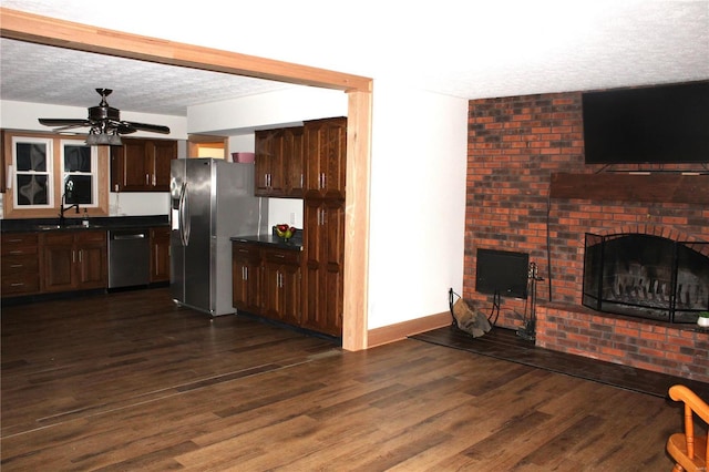 kitchen with a fireplace, dark wood finished floors, stainless steel appliances, dark countertops, and a textured ceiling