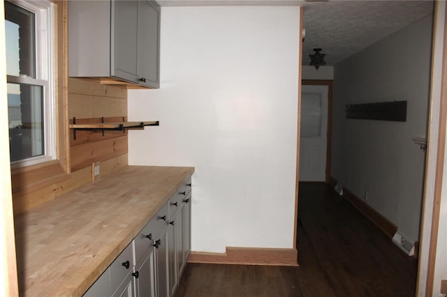 kitchen featuring a textured ceiling, baseboards, dark wood-type flooring, and butcher block countertops