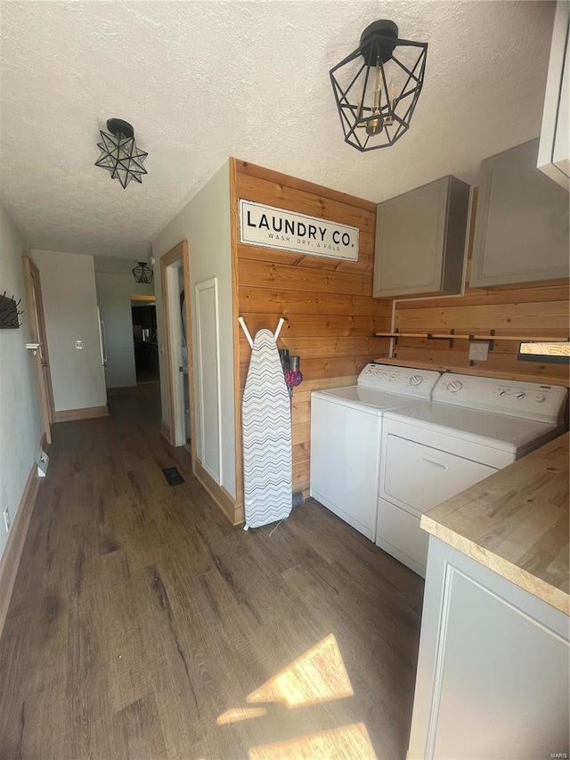 laundry room featuring a textured ceiling, wood walls, wood finished floors, cabinet space, and washing machine and clothes dryer