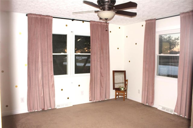 empty room featuring carpet floors, visible vents, a textured ceiling, and a ceiling fan