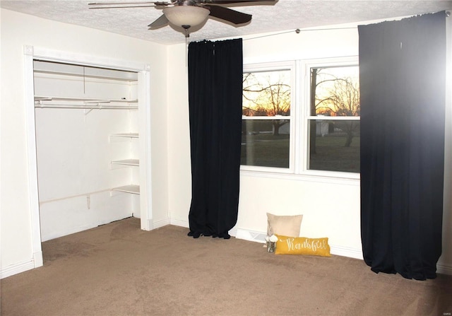 unfurnished bedroom with a closet, carpet flooring, ceiling fan, a textured ceiling, and baseboards