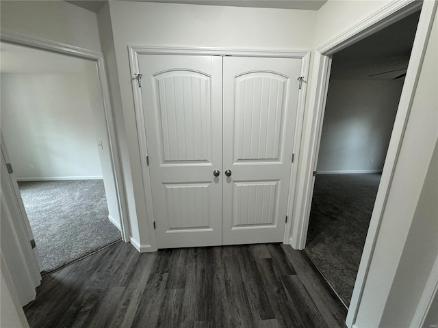 corridor featuring dark colored carpet, dark wood-style flooring, and baseboards