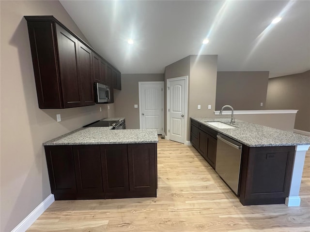 kitchen featuring stainless steel appliances, a sink, a peninsula, and light stone counters