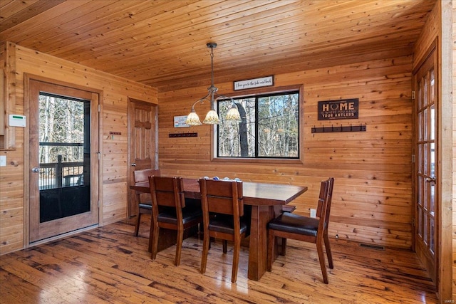 dining space with wooden ceiling, wooden walls, and light wood finished floors