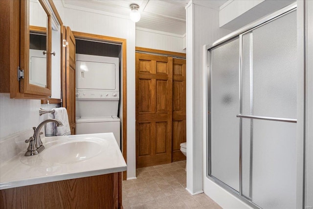 bathroom with vanity, stacked washing maching and dryer, a shower stall, and toilet