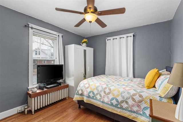 bedroom featuring wood finished floors, baseboards, a textured wall, and ceiling fan