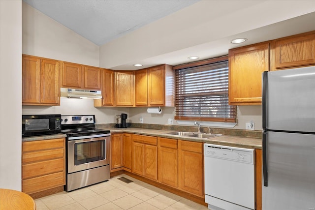 kitchen with light tile patterned floors, vaulted ceiling, stainless steel appliances, under cabinet range hood, and a sink