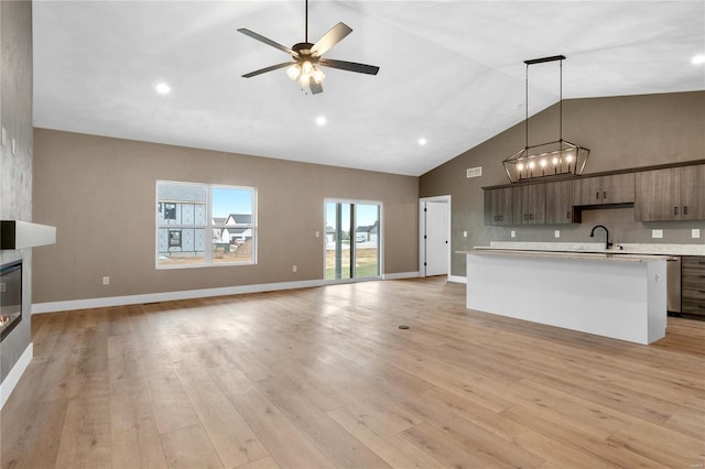 kitchen with light wood-type flooring, a sink, open floor plan, a large fireplace, and light countertops