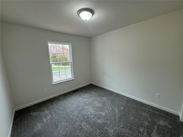 empty room featuring visible vents, dark carpet, and baseboards