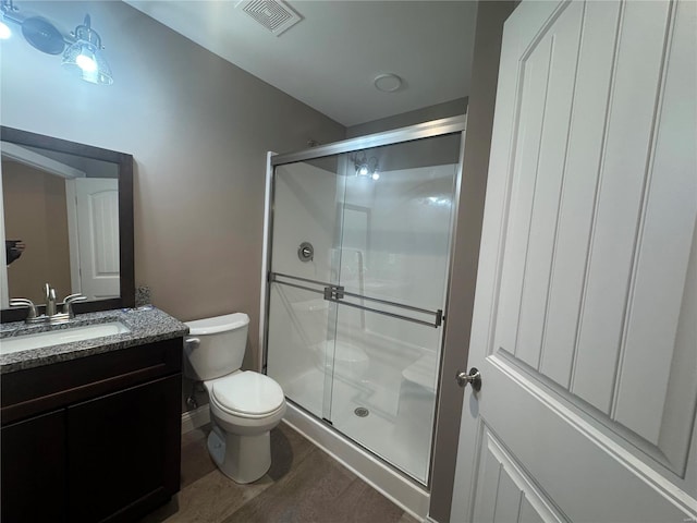 bathroom with toilet, wood finished floors, vanity, visible vents, and a stall shower