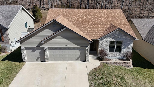 view of front of house with a shingled roof, concrete driveway, a front yard, a garage, and stone siding