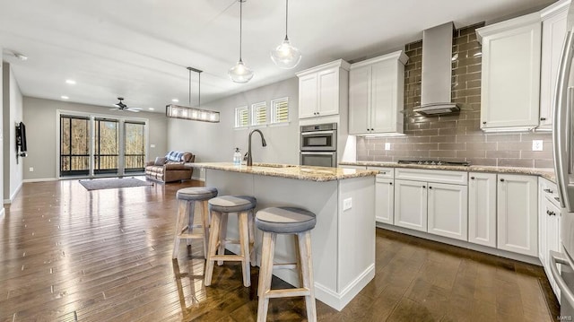 kitchen with dark wood finished floors, double oven, decorative backsplash, wall chimney exhaust hood, and a sink