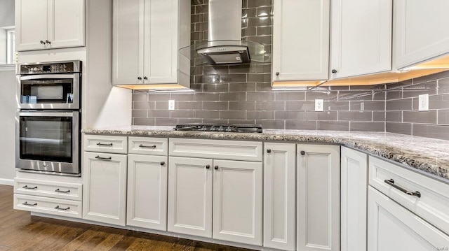 kitchen with light stone countertops, stainless steel appliances, dark wood-type flooring, wall chimney exhaust hood, and backsplash