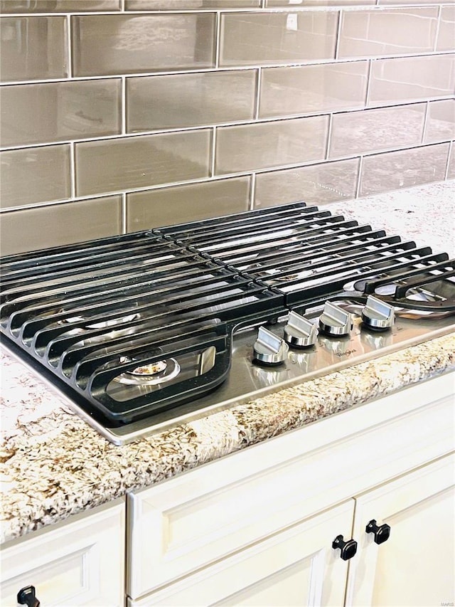 interior details featuring decorative backsplash, light stone countertops, white cabinets, and stainless steel gas cooktop