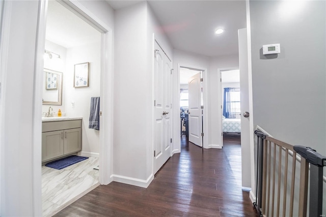 corridor featuring dark wood finished floors, a sink, and baseboards