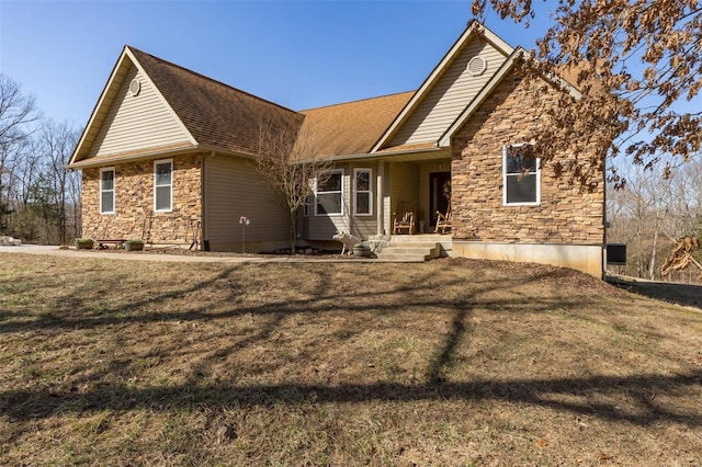 rear view of house featuring stone siding, a lawn, and a shingled roof