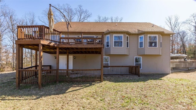 rear view of property featuring a deck, a lawn, and roof with shingles