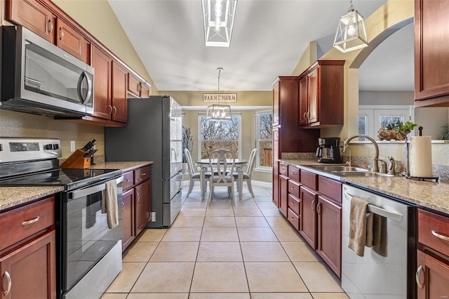 kitchen with a sink, reddish brown cabinets, appliances with stainless steel finishes, and vaulted ceiling