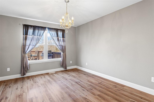 spare room with a notable chandelier, baseboards, and wood finished floors