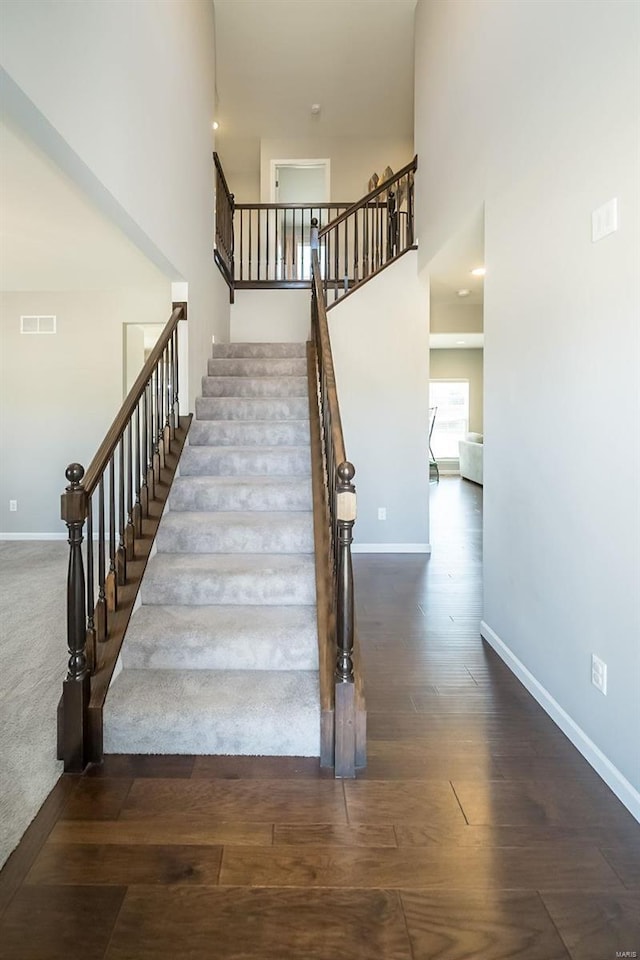 stairs with a high ceiling, wood finished floors, visible vents, and baseboards