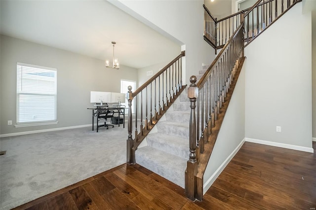 stairs with wood finished floors, baseboards, a high ceiling, a notable chandelier, and carpet flooring