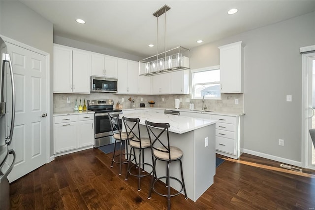 kitchen with a breakfast bar area, a kitchen island, dark wood-style flooring, a sink, and appliances with stainless steel finishes