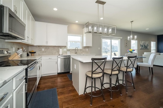 kitchen with a breakfast bar area, dark wood-style floors, a kitchen island, appliances with stainless steel finishes, and backsplash