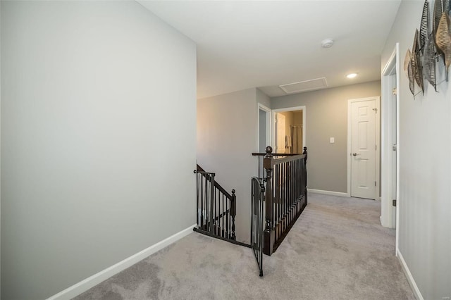 hall with an upstairs landing, light colored carpet, and baseboards