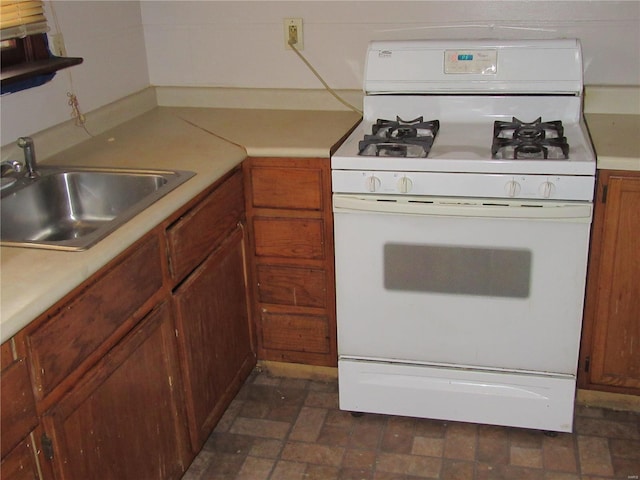 kitchen featuring brown cabinetry, light countertops, a sink, and white gas range