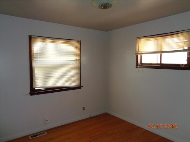 unfurnished room featuring baseboards, visible vents, and wood finished floors