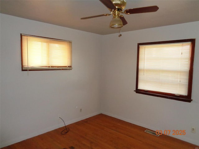 unfurnished room with visible vents, a ceiling fan, wood finished floors, plenty of natural light, and baseboards