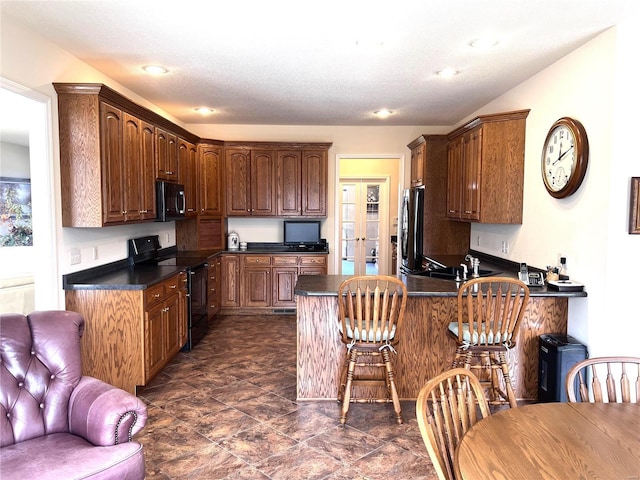 kitchen with dark countertops, black appliances, a peninsula, and a kitchen breakfast bar