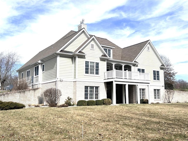 back of house with a chimney, brick siding, a yard, and a balcony