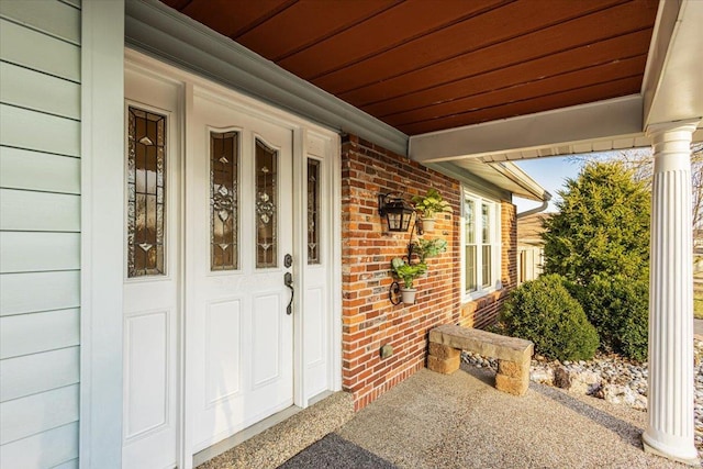 doorway to property with a porch and brick siding