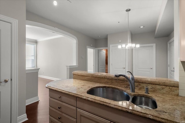 kitchen with baseboards, light stone counters, dark wood-style flooring, pendant lighting, and a sink