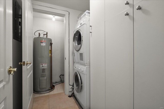 laundry area featuring laundry area, light tile patterned flooring, stacked washing maching and dryer, and electric water heater